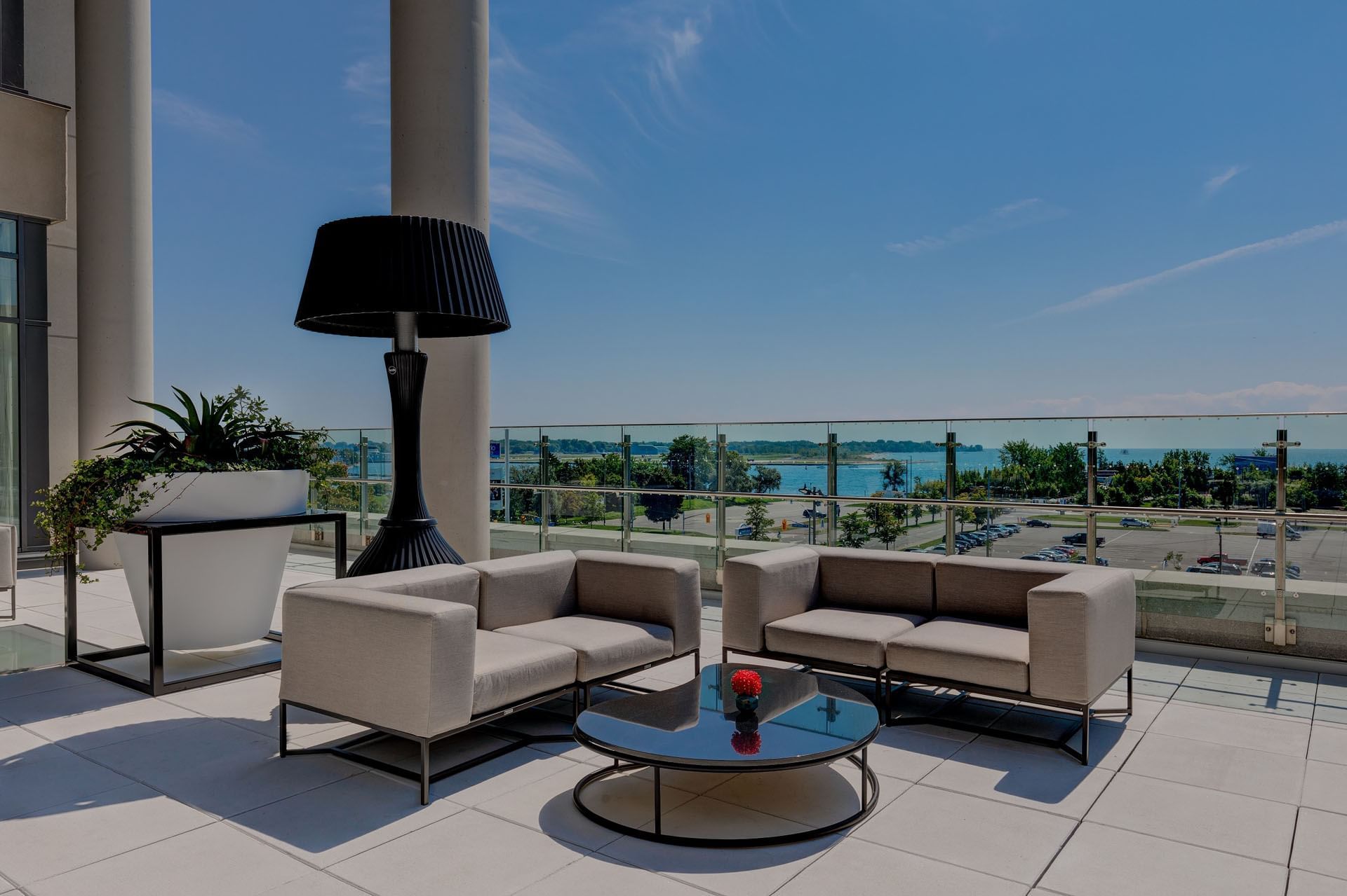 Marina Terrace with gray sofas flank a round glass table by a black lamp overlooking the marina at Hotel X Toronto