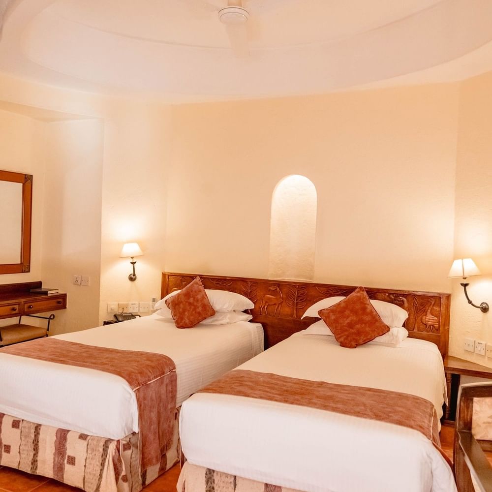 Two twin beds with wooden headboards and warm decor in a Standard Twin Room at Arusha Serena Hotel, Arusha.