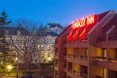 Side view of the Embassy Inn Victoria building at dusk with a prominent red neon sign