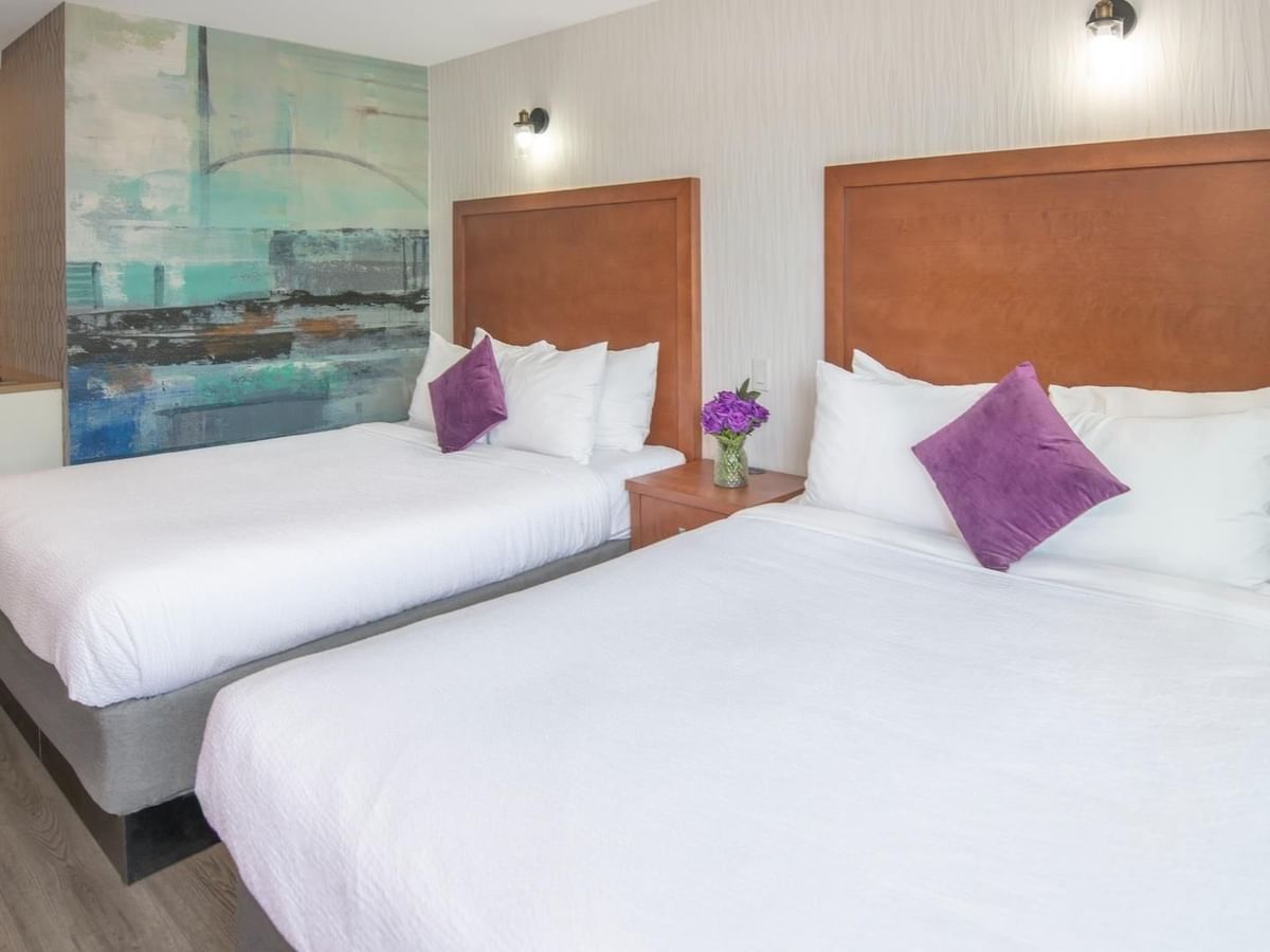 Two queen beds with white linens and purple pillows, wooden headboards and a colorful mural on the wall.