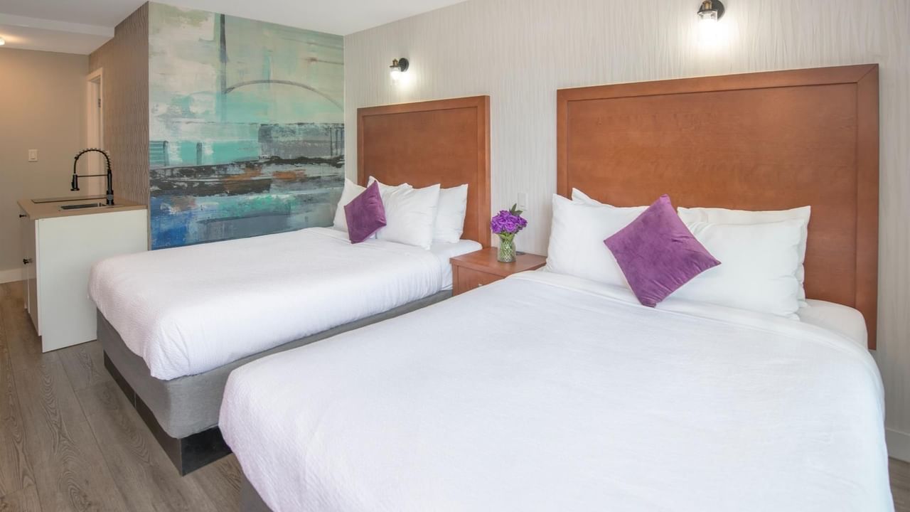 Two queen beds with white linens and purple pillows, wooden headboards and a colorful mural on the wall.