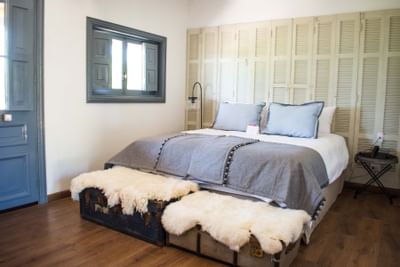 Large bed with blue pillows by a fur-covered trunk under a shuttered window in the room at NOI Blend Colchagua