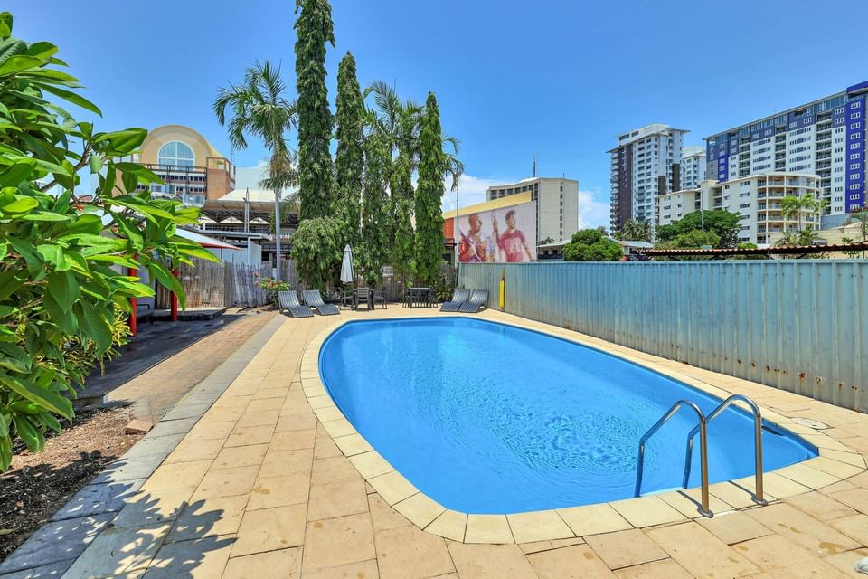 Outdoor pool area with loungers and a table set at Darwin Poinciana Inn