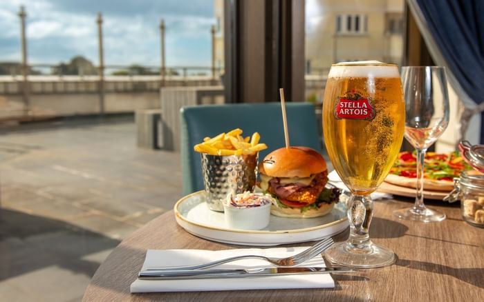 Plate of food with fries, burger, coleslaw and Stella Artois beer at The View Hotel Eastbourne