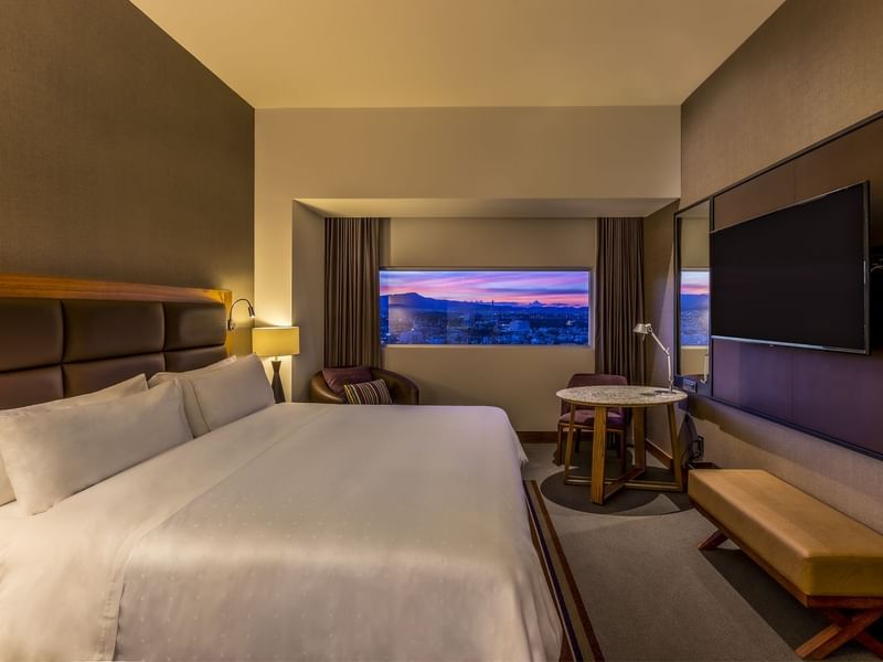 Deluxe Room with a large bed, TV, round table, and window framing a cityscape at Fiesta Americana San Luis Potosí