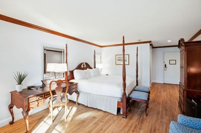 Four-poster bed with two benches near wooden desk with chair beside tall armoire in guest room at Avon Old Farms Hotel
