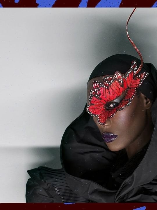 Grace Jones in black outfit and red butterfly mask.