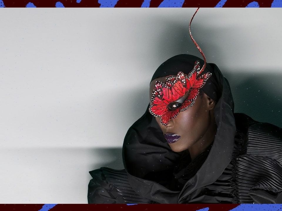 Grace Jones in black outfit and red butterfly mask.