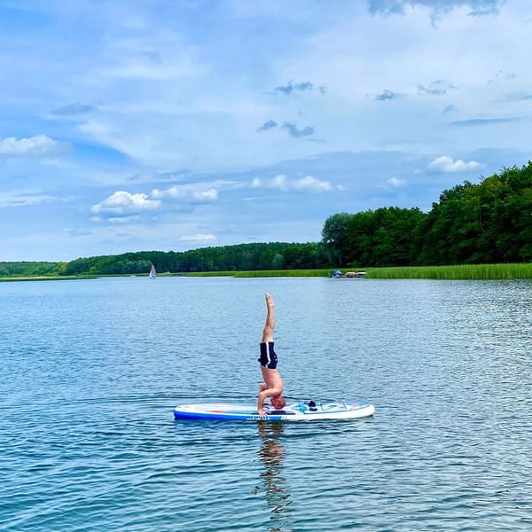 Person performing a headstand on a paddleboard in calm lake waters near the Falkensteiner Hotels & Residences