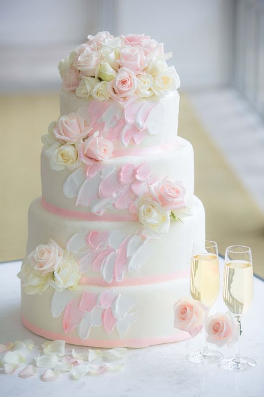 Three-tiered wedding cake adorned with pink and white roses and two champagne flutes beside it at Park Hyatt Saigon