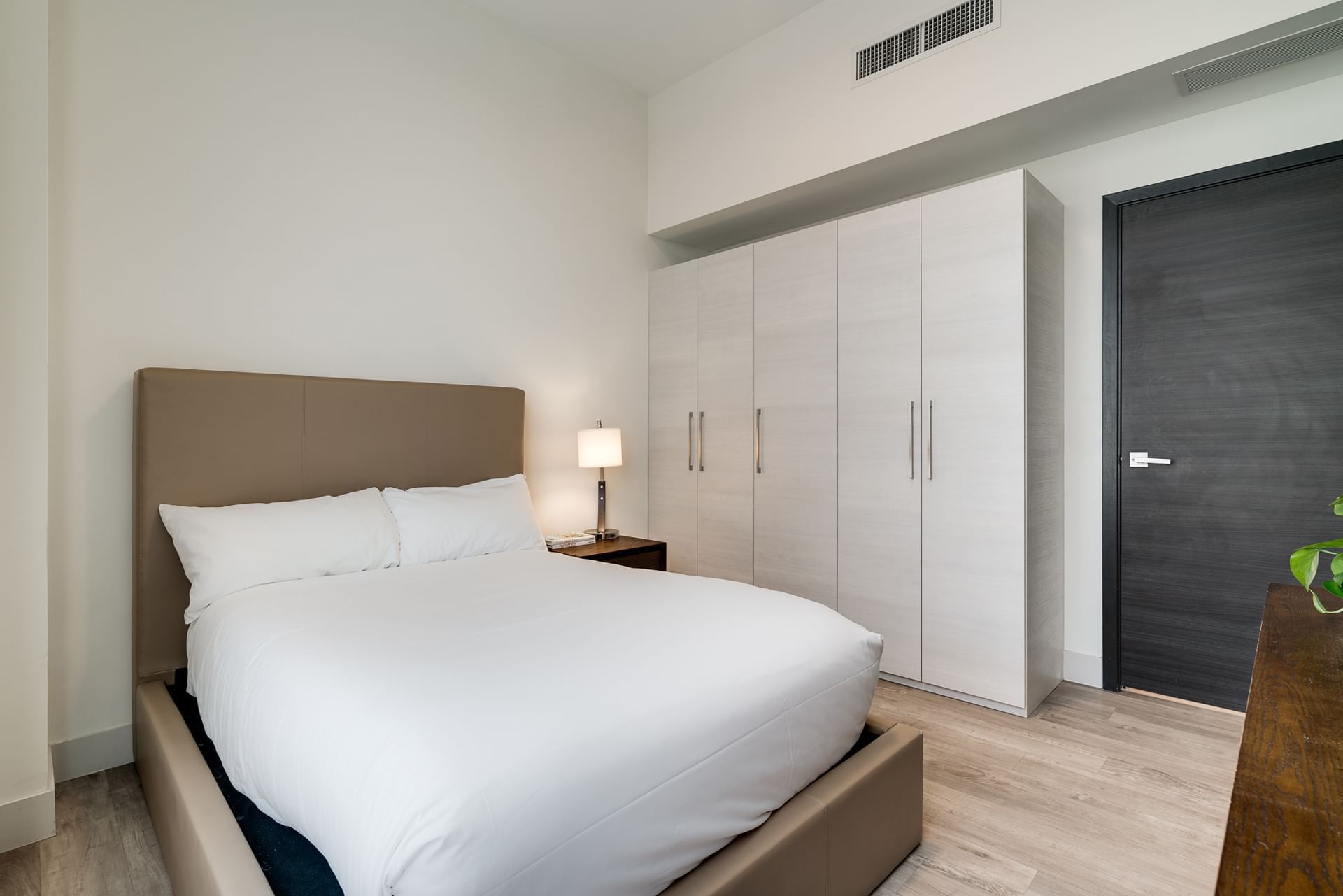 A hotel room with a bed, wardrobe, lamp, and door.