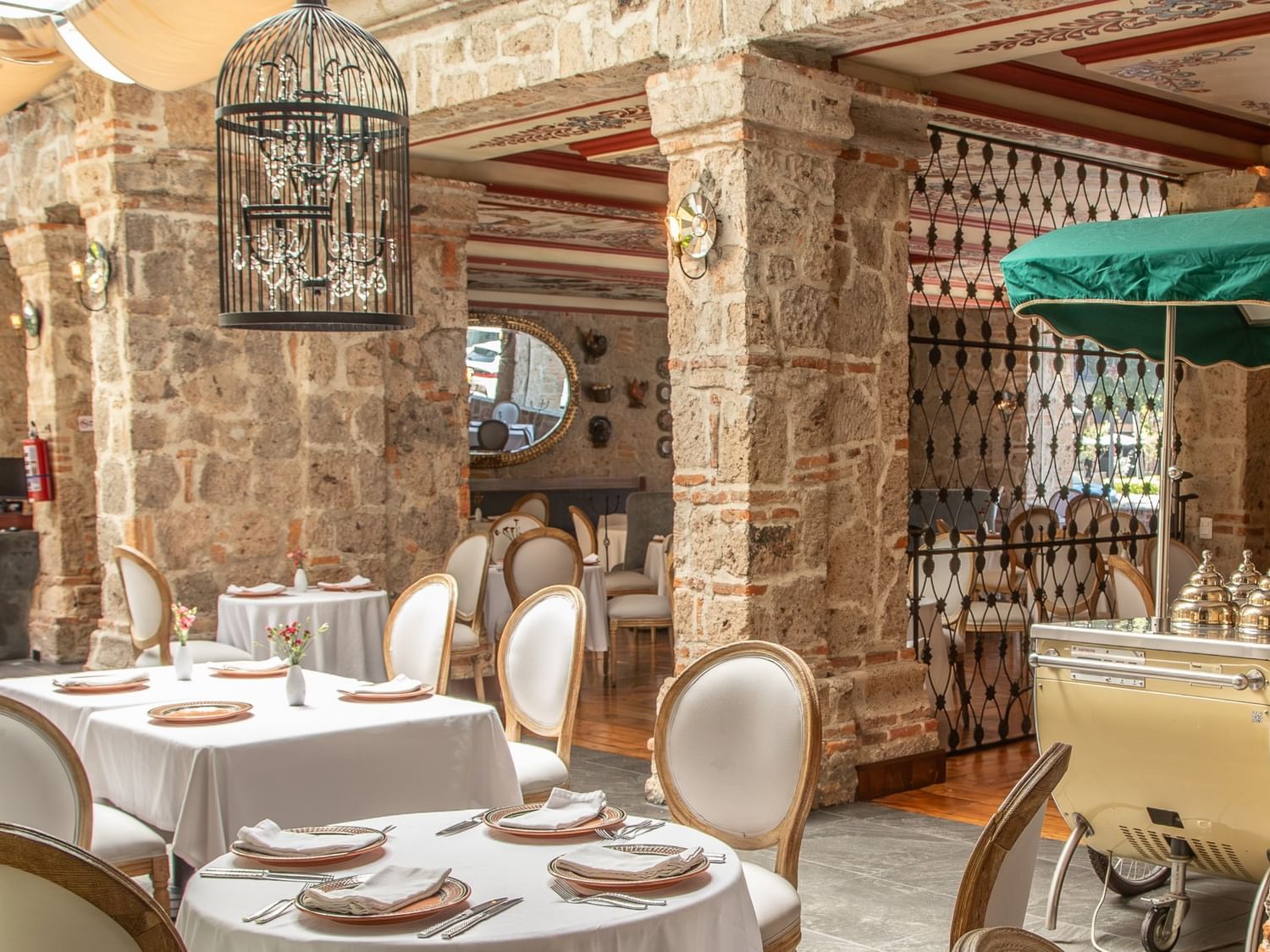 Tierra Mia restaurant with white-clothed tables, exposed stone columns, and decorative birdcage at Quinta Real Guadalajara