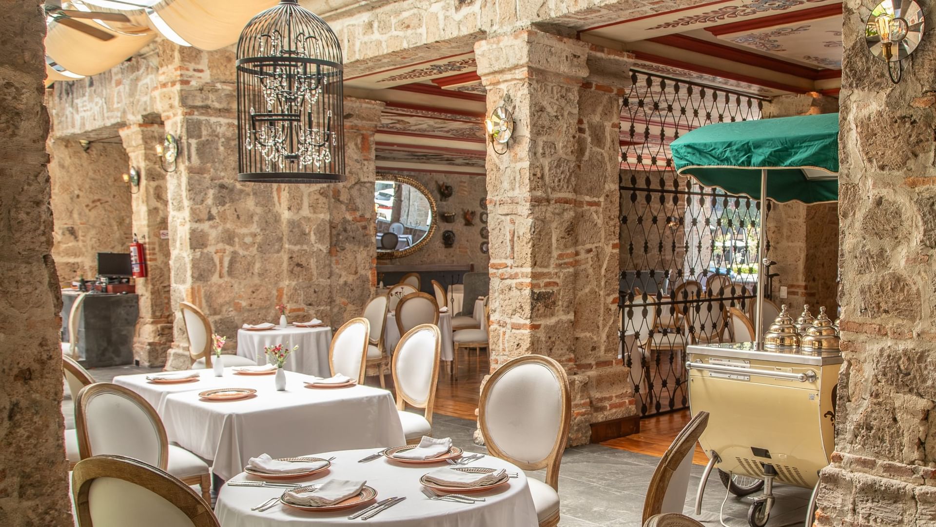 Tierra Mia restaurant with white-clothed tables, exposed stone columns, and decorative birdcage at Quinta Real Guadalajara