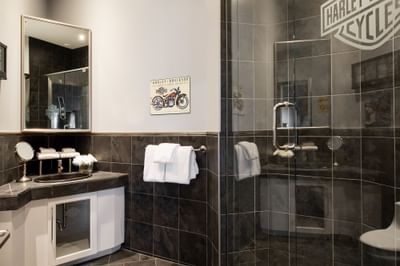 Bathroom vanity with amenities, towel rack & shower area in Queen Premiere Easy Rider at Retro Suites Hotel