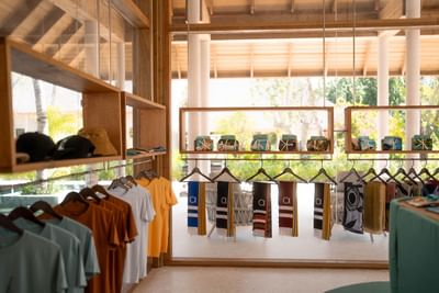 Stylish boutique at Ananea Madivaru Maldives with colorful t-shirts and patterned scarves on wooden hangers, lit by sunlight