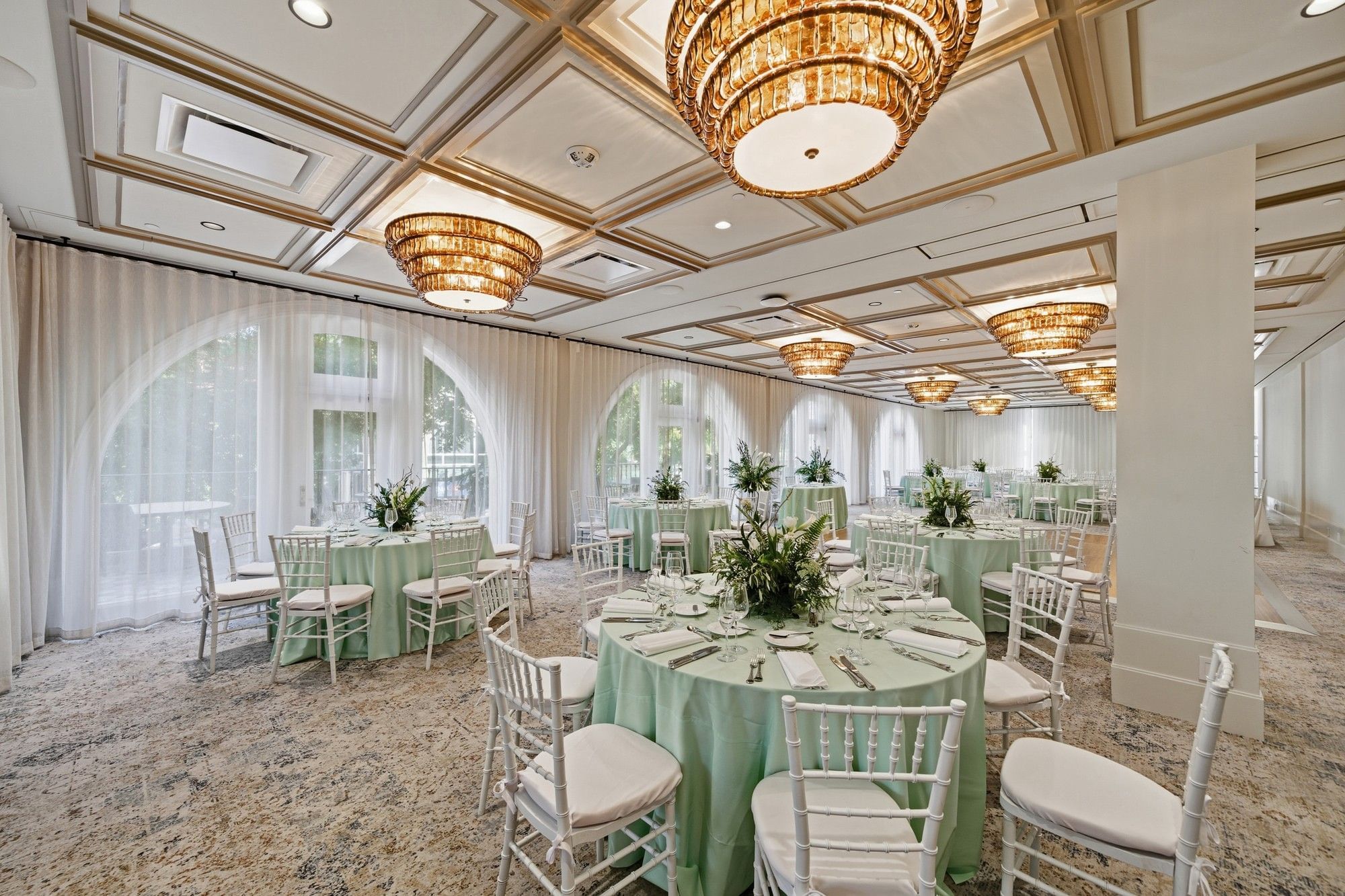 Elegantly set tables and chairs in a grand hall with large chandeliers at El Prado Palo Alto