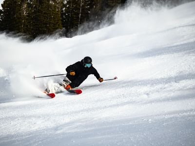 Skier in black and orange snow gear skiing down a snowy slope at Elevation Resort Spa