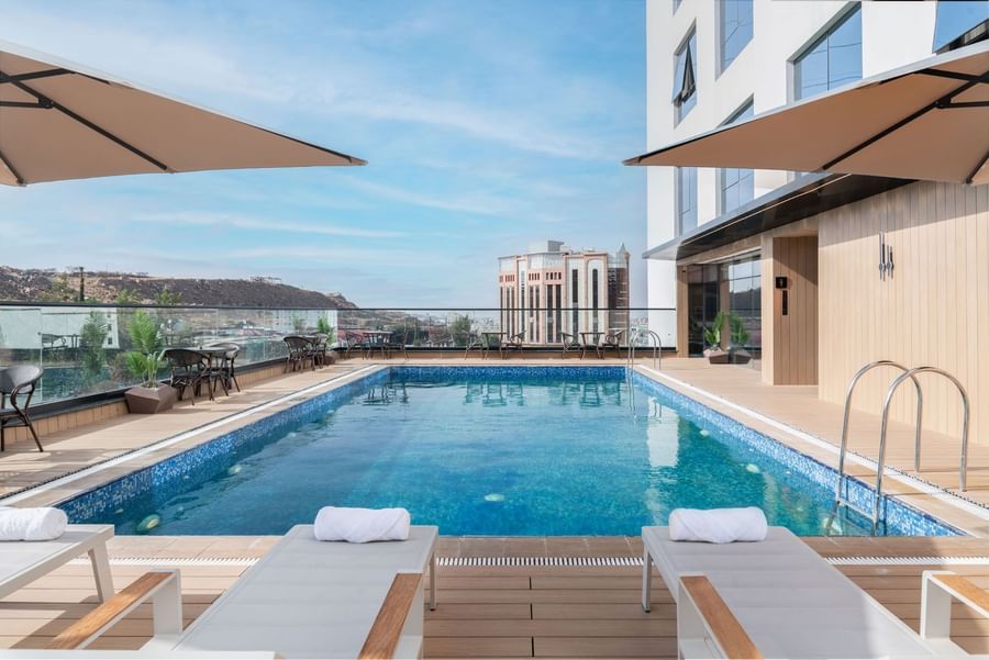 Sun loungers and dining tables set by the rooftop pool and city view at Warwick Al Taif Hotel