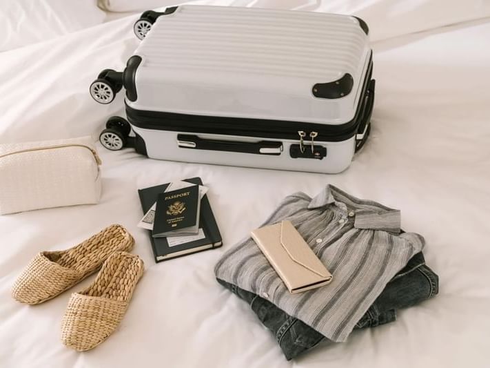 A white suitcase, a US passport, and vacation clothes on a bed, things to do in South Beach Miami at Kenmore Village Hotel