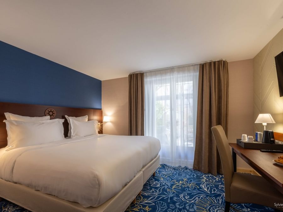 Chambre élégante avec lits blancs et bureau éclairé chez Hôtel Le Yachtman.