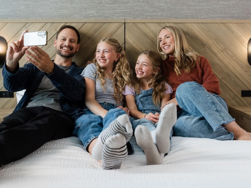 Family of four smiling and taking a selfie on a Sandman Hotel bed