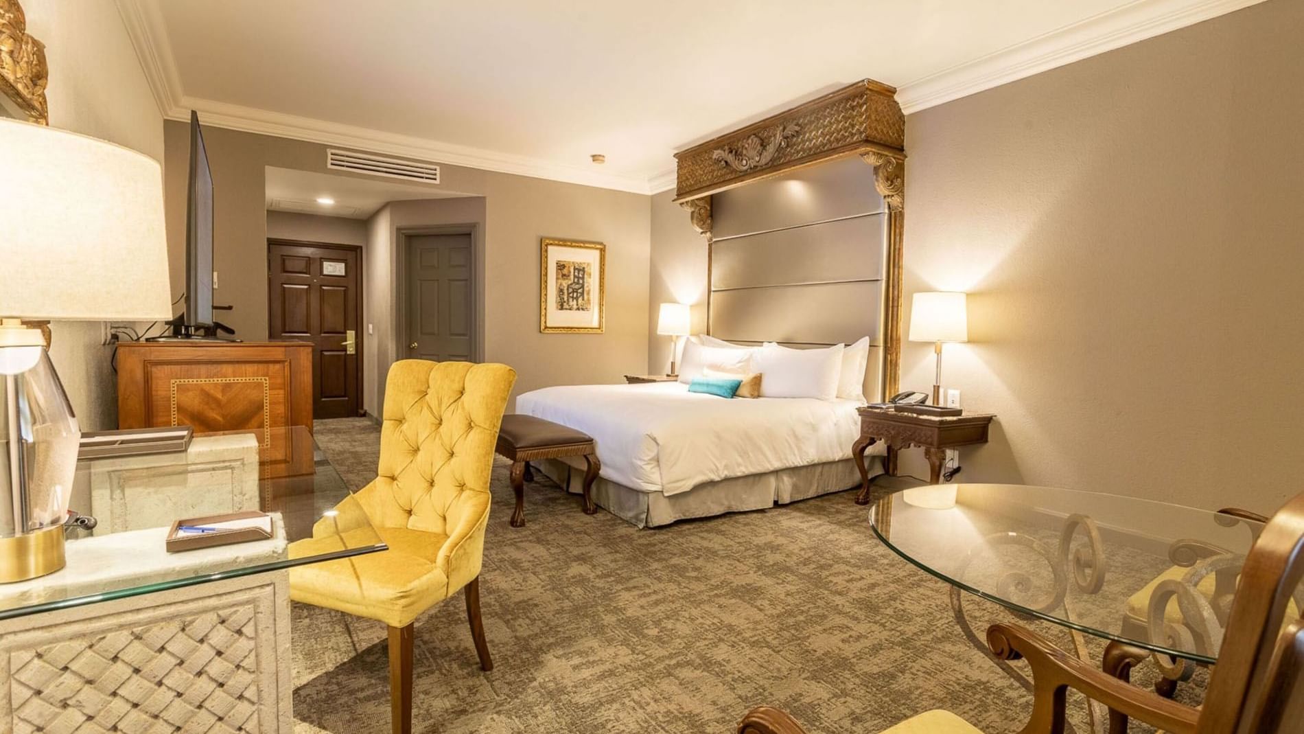 King Master Suite featuring a yellow tufted chair, glass desk, and a king-sized bed at Quinta Real Monterrey