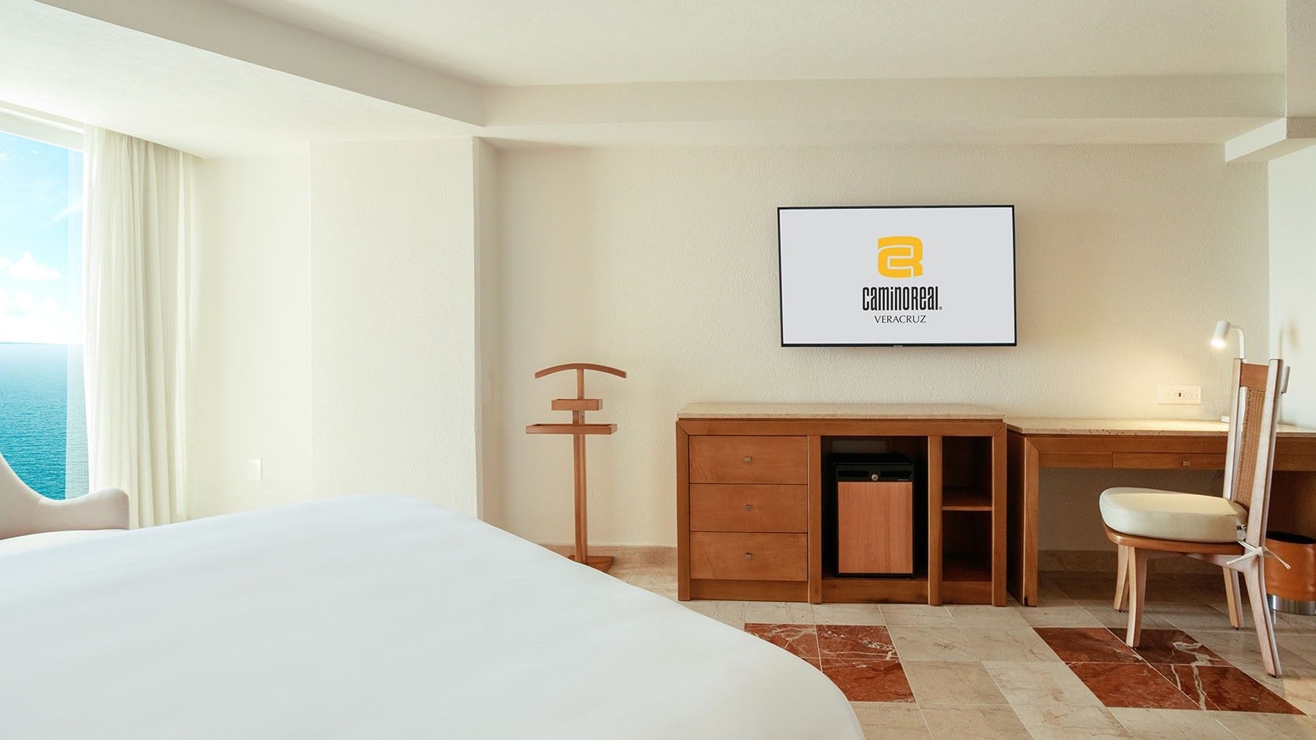 Minimalist King Deluxe room detail showing a wooden dresser with a mini-fridge and a valet stand at Camino Real Veracruz