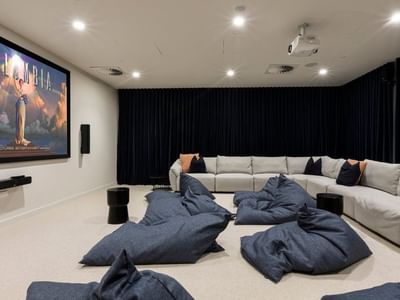 Home theater with large screen, projector, L-shaped couch, bean bags, and black curtains.
