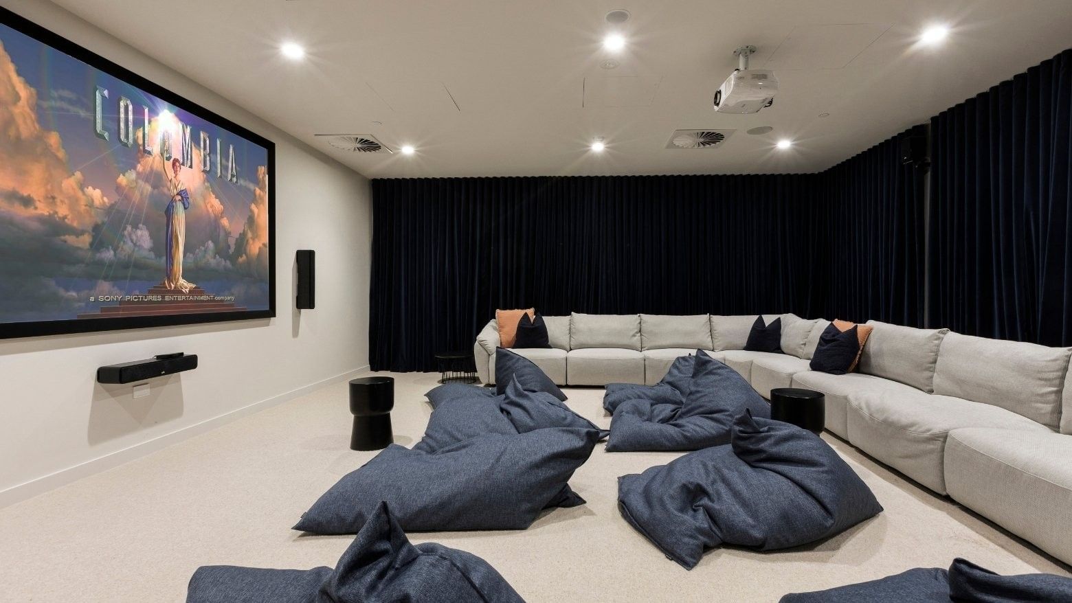 Home theater with large screen, projector, L-shaped couch, bean bags, and black curtains.