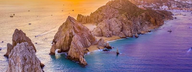 Majestic rock formations and beaches at sunset, viewed from the ocean near the Marquis Los Cabos Resort.
