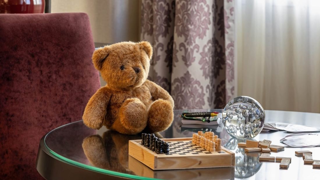 Teddy bear and chess set on a glass table by purple curtains in Family Room – Two Queen Beds at Warwick Paris Champs Elysées