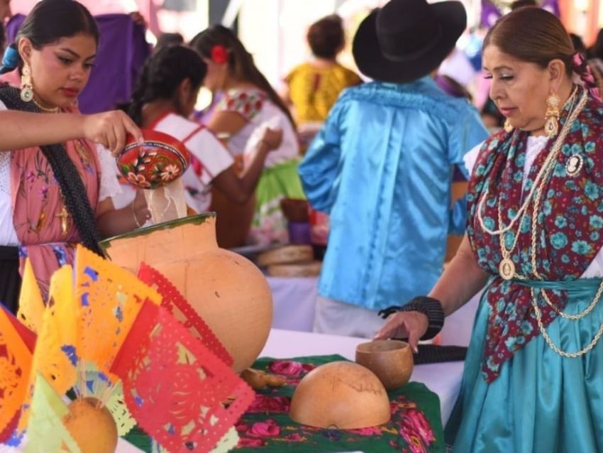 Women in traditional attire serve food from clay pots at a festive market stall at Camino Real Fashion Drive, Monterrey