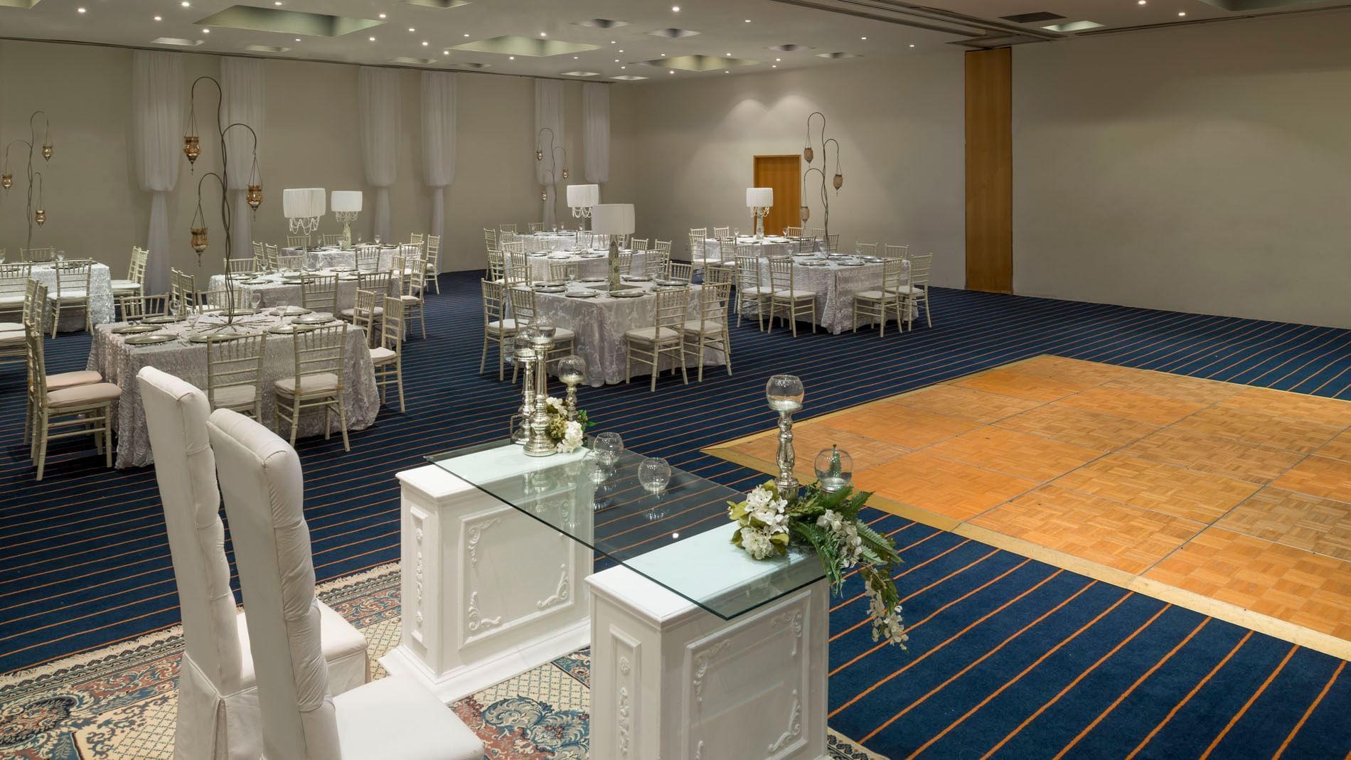 The banquet hall set for a gala with white linens, a dance floor, and striped carpets at Real Inn Nuevo Laredo