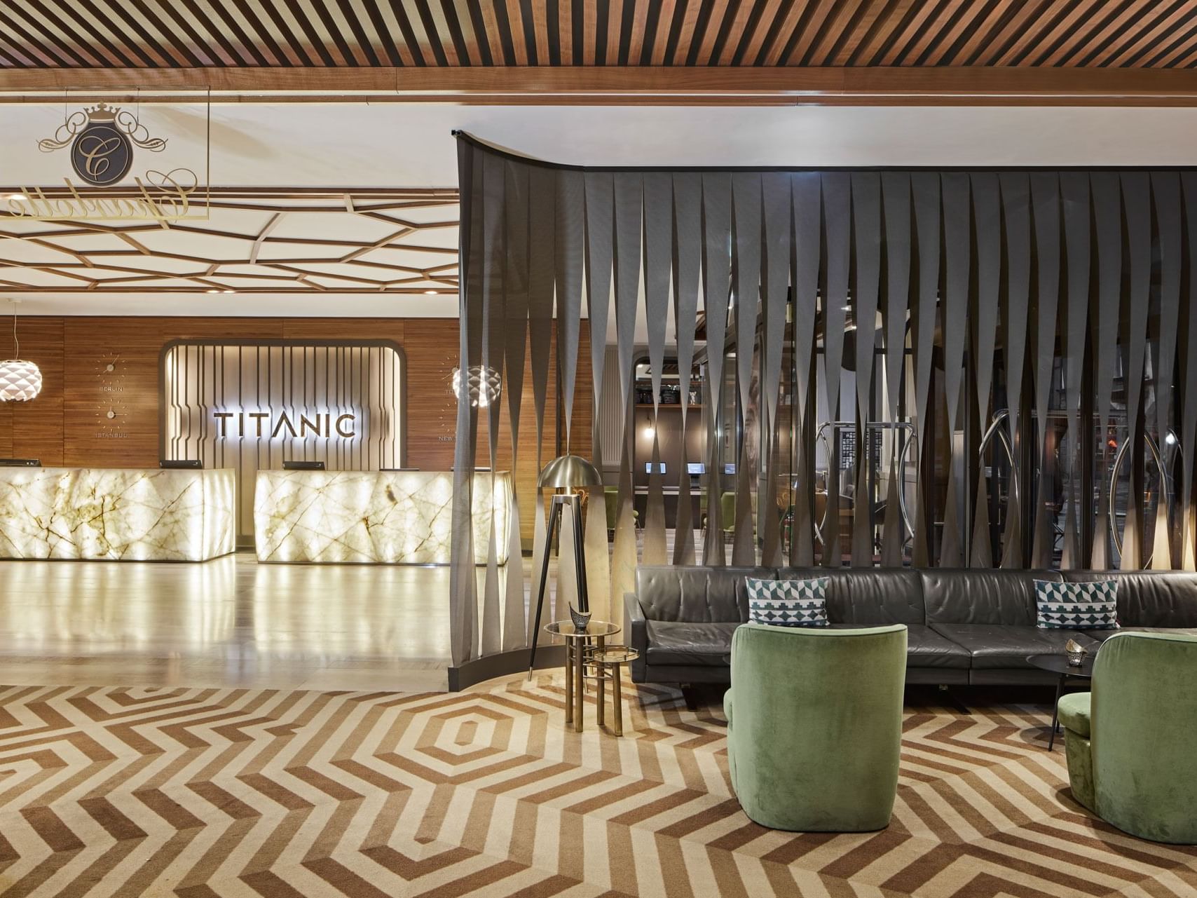Moderne Lobby mit geometrischem Teppich, schwarzen Sofas, grünen Sesseln und Empfangstheke – Titanic Chaussee Berlin.