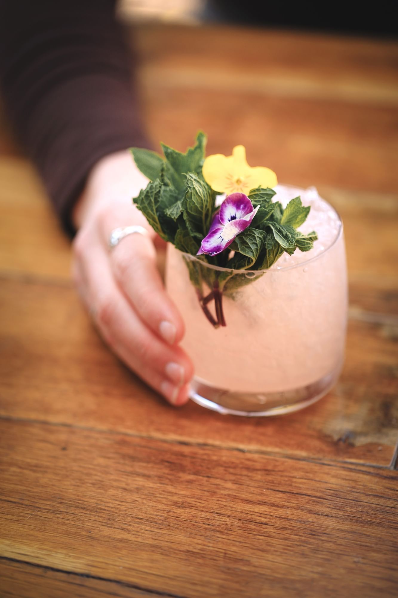 Lorem ipsum Hand holding pink cocktail topped with mint, a yellow flower and purple flower