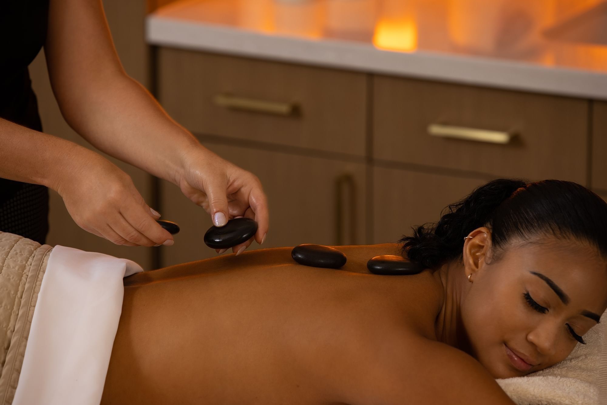 Therapist placing warm stones on a guest’s back by wooden cabinets in a spa at Warwick Melrose Dallas