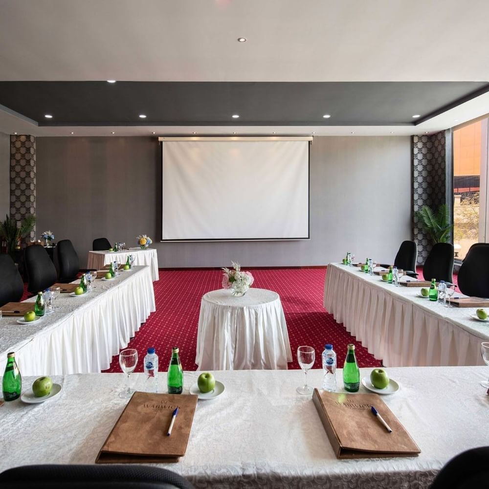 Long tables and black chairs surrounding a projector screen by a window in Crystal B at Warwick Al Jubail