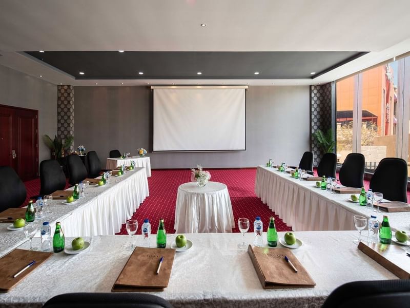 Long tables and black chairs surrounding a projector screen by a window in Crystal B at Warwick Al Jubail