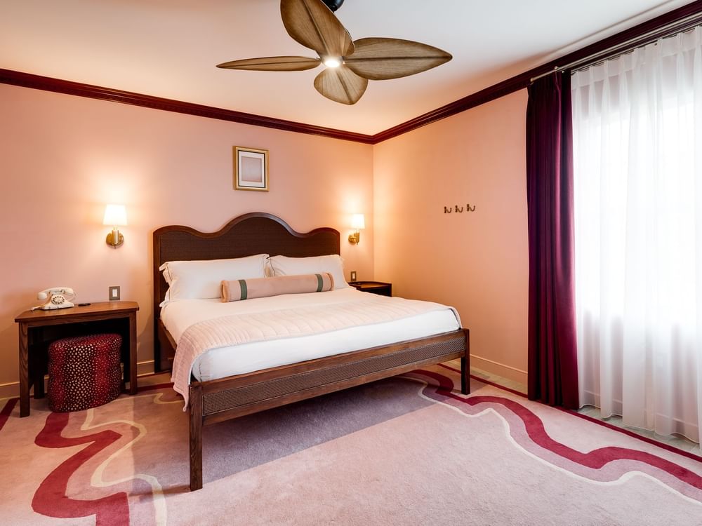 A hotel room with a king-sized bed, nightstands, and a window with curtains.