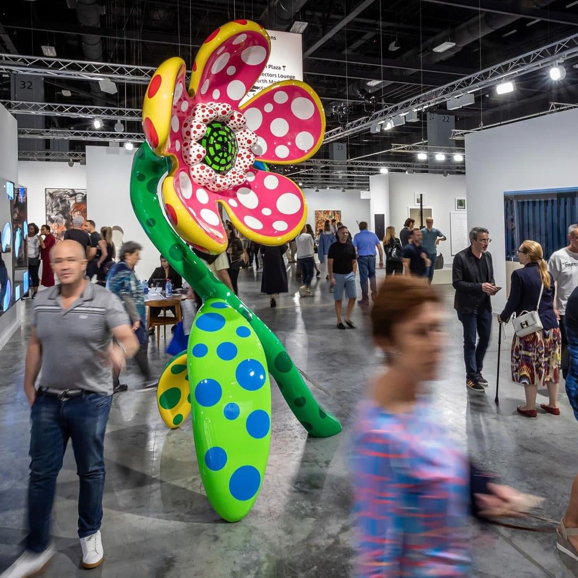 Colored large polka-dot flower sculpture by Yayoi Kusama inside a busy modern art fair near Tradewinds Apartment Hotel