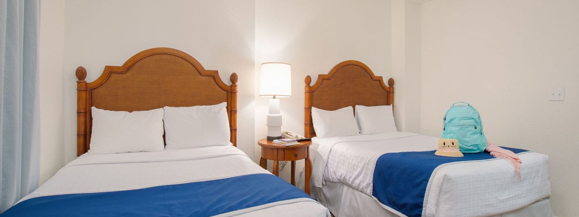 A hotel room with two twin beds, wooden headboards, and white bedding with blue spreads.