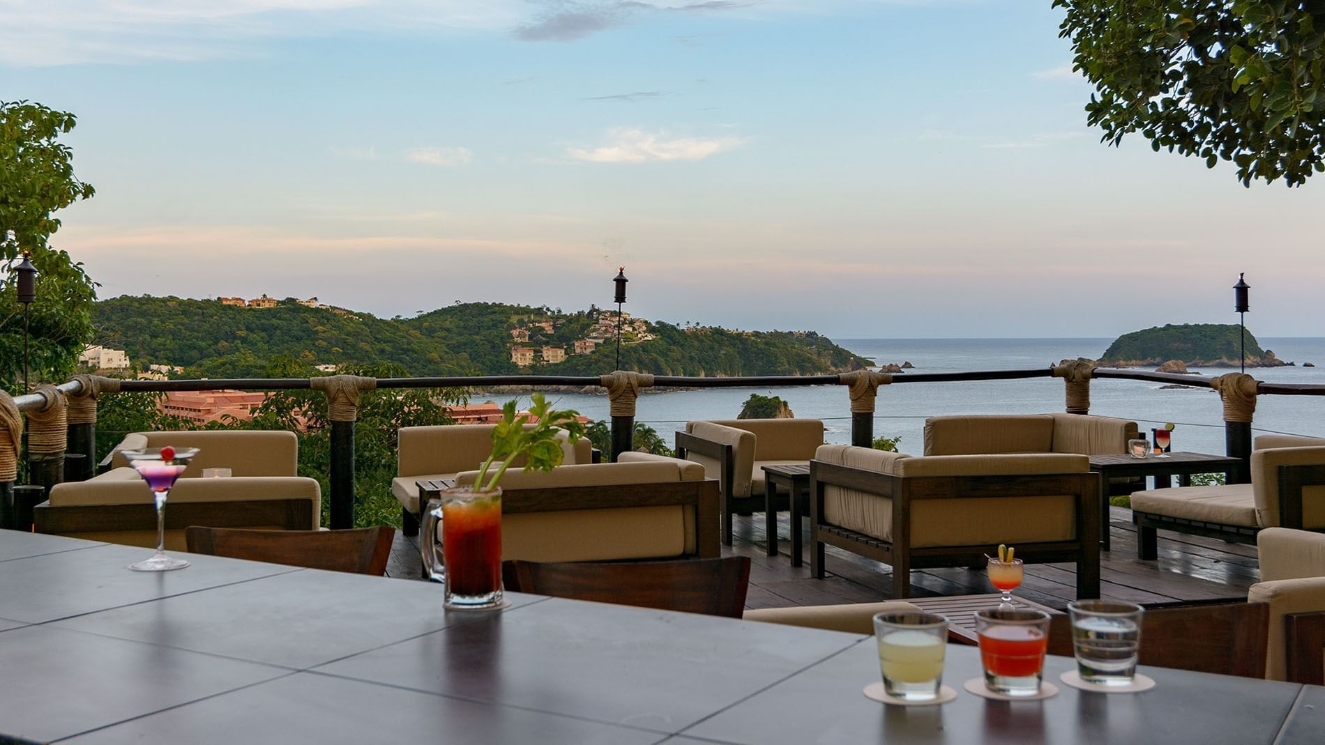 Sky Lounge bar area featuring outdoor sofas by cocktails under tiki torches surrounding the bay at Quinta Real Huatulco
