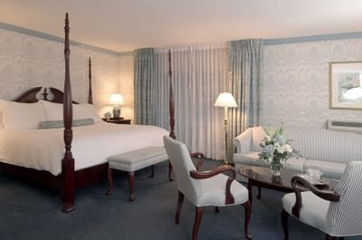 Four-poster bed beside striped armchairs and sofa in spacious guest room at Farmington Inn and Suites
