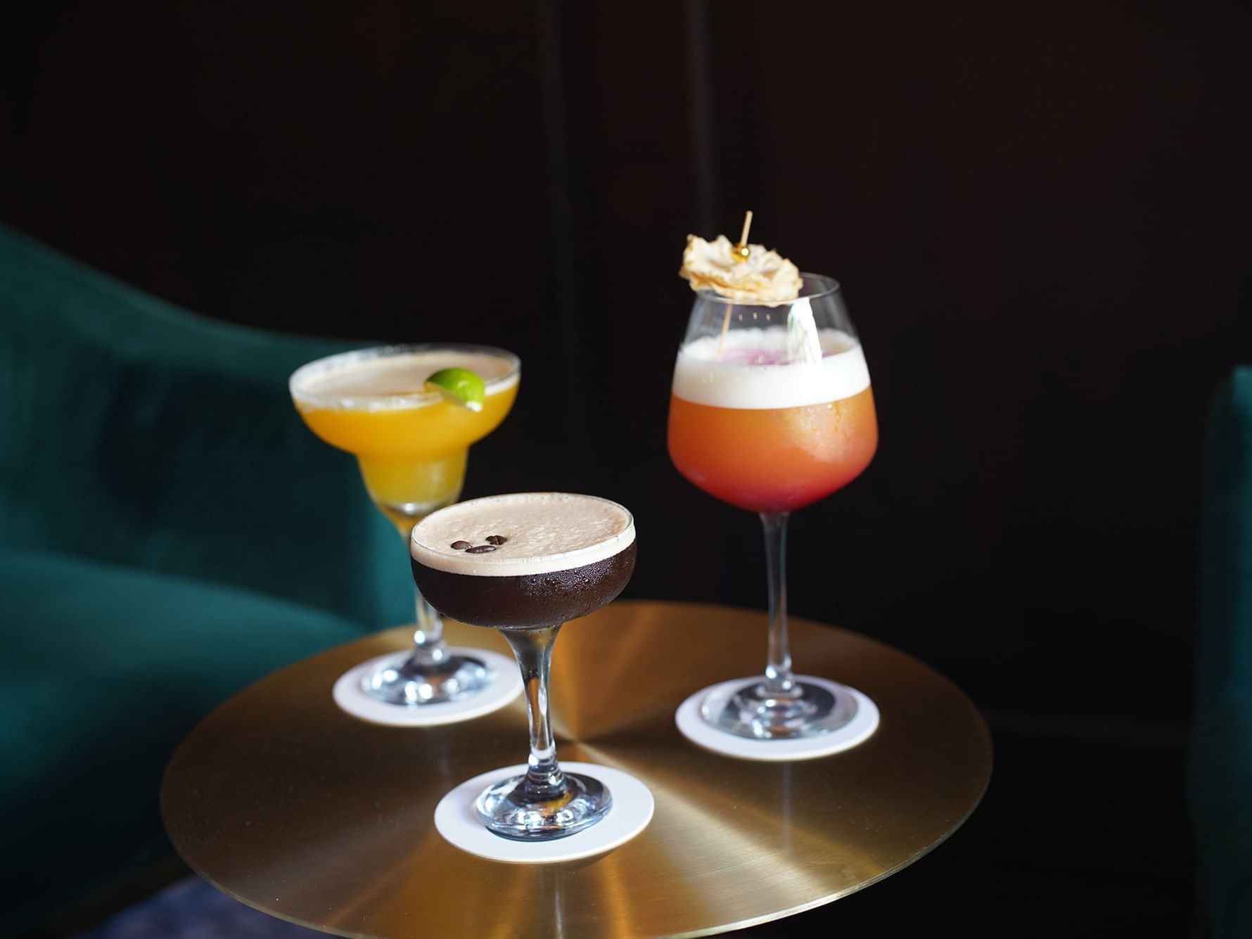 Three colorful cocktails garnished and set on a gold table in Mingles Bar & Lounge at Courtleigh Hotel & Suites