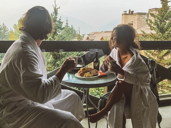 A couple in bathrobes having breakfast on a balcony in a room at Blackcomb Springs Suites