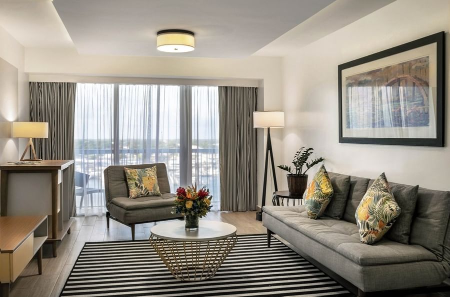 One Bedroom Harbourfront Suite with grey couch by a round table under a ceiling light at Warwick Paradise Island Bahamas