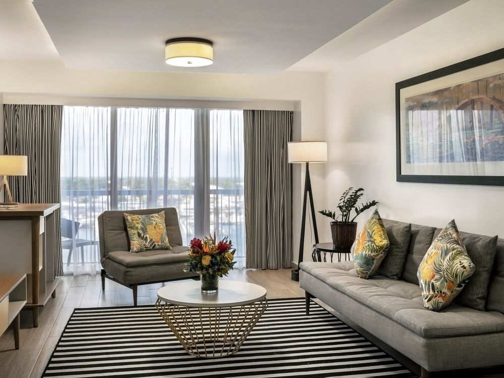 One Bedroom Harbourfront Suite with grey couch by a round table under a ceiling light at Warwick Paradise Island Bahamas