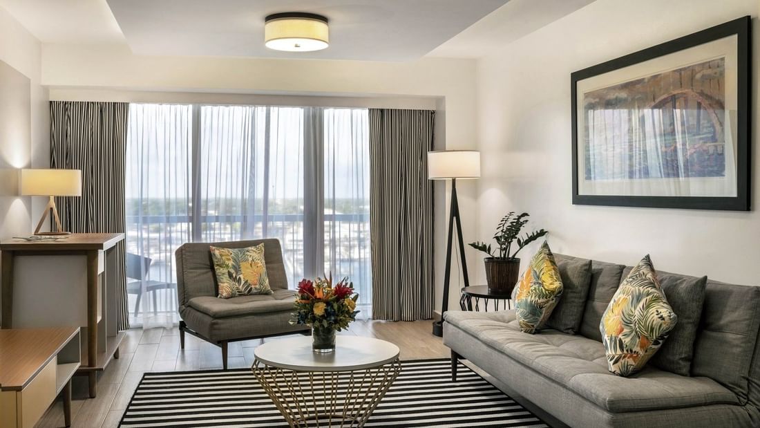 One Bedroom Harbourfront Suite with grey couch by a round table under a ceiling light at Warwick Paradise Island Bahamas