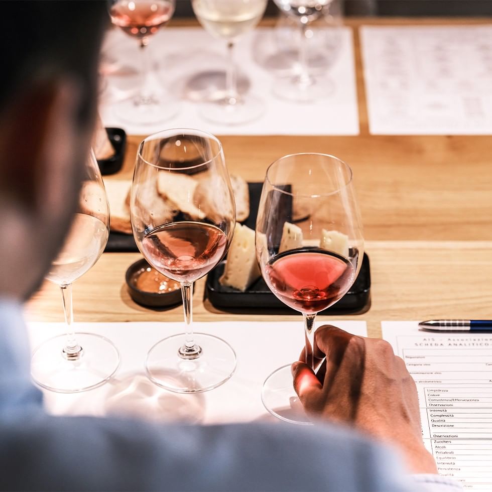 Mann hält ein Weinglas mit rotem Wein vor einem Tisch mit Käse und weiteren Gläsern.