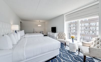 Two Queen beds near and a sitting area near a large window in the Queen Studio+ Cape May hotel room